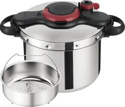 A stainless steel pressure cooker with a steamer basket in front of it, set against a white background.