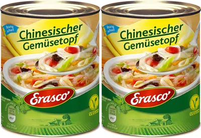 Two cans of Erasco Chinesischer Gemüsetopf (Chinese Vegetable Stew) are shown side-by-side against a background that transitions from yellow at the top to green at the bottom, with a subtle illustration of fields and houses.