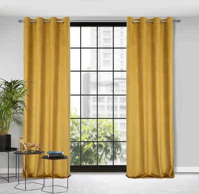 A pair of yellow curtains hanging in front of a large window with a grid pattern. There are two small black tables in the foreground with a plant and some books.