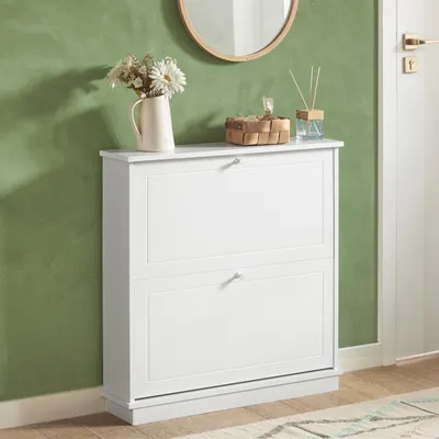A white shoe cabinet with two drawers is shown against a green wall.