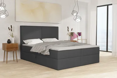 A bedroom scene featuring a large bed with a headboard and bedding, a bedside table with decorative items, and a large window in the background.