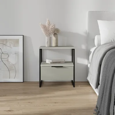 A modern nightstand with a drawer and shelf, placed next to a bed in a bedroom setting.