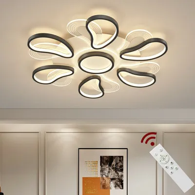 A modern ceiling lamp with multiple curved elements, illuminated and casting shadows on the ceiling. A remote control is shown in the foreground, with a red signal icon above it.