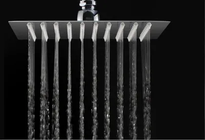 A close-up shot of a square shower head with water streaming from multiple nozzles against a black background.