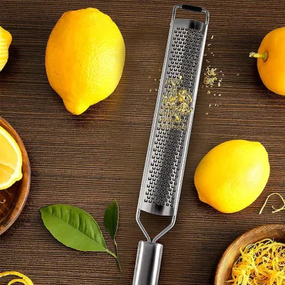 A grater with lemon zest on it, surrounded by lemons and lemon leaves on a wooden surface.