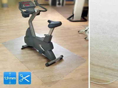 An exercise bike is placed on a transparent mat on a wooden floor.