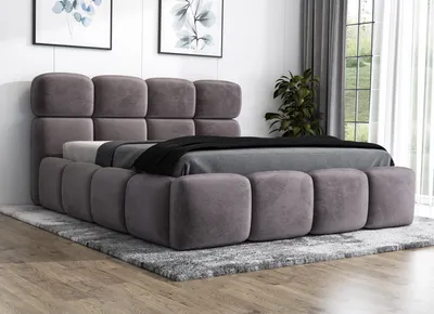 A modern upholstered bed with a headboard and footboard, placed on a rug in a room.