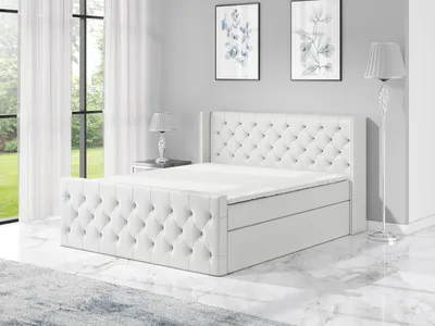 A white boxspring bed with a tufted headboard and footboard is shown in a bedroom setting.