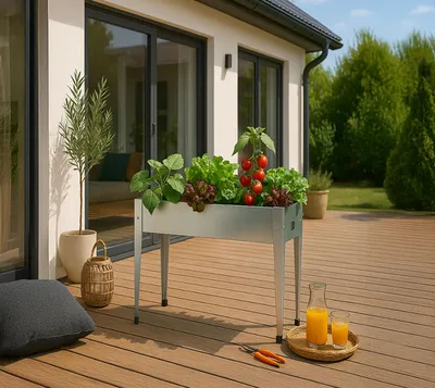 A raised metal planter filled with vegetables and tomatoes sits on a wooden deck next to a house.