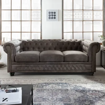 A Chesterfield sofa in a living room setting with large windows in the background.