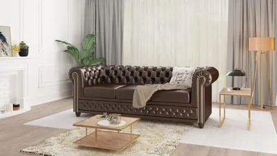 A brown Chesterfield sofa is shown in a living room setting with a coffee table, lamp, and fireplace.