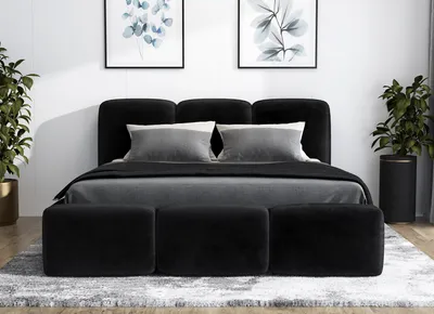 A black upholstered bed with a headboard and three ottomans in front, set in a bedroom with artwork on the wall and plants.