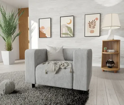 A modern living room scene with a gray cord fabric armchair, decorative wall art, a plant, and a wooden side table with a lamp.