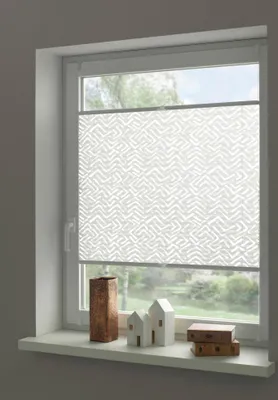 A white pleated blind with a geometric pattern is installed on a window. Decorative items are placed on the windowsill below.