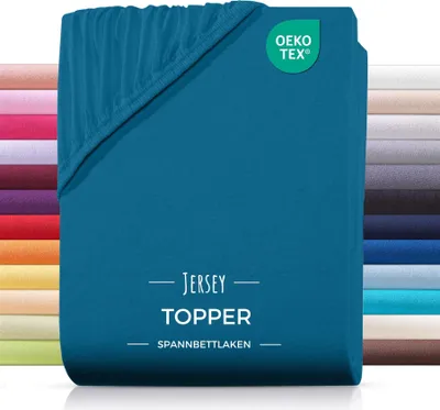 A teal-colored fitted sheet or topper is shown folded, with a stack of other colored sheets in the background. A certification logo is visible in the top right corner.