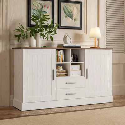 A white and brown sideboard with two doors and three drawers, decorated with two framed pictures and a lamp on top.