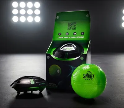 A Smart Ball Soccer Bot and its packaging are displayed on a dark surface with bright lights in the background.