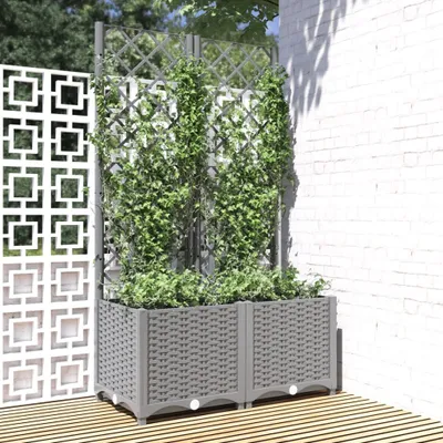 Two grey planters with green vines in front of a white brick wall and a decorative white panel.