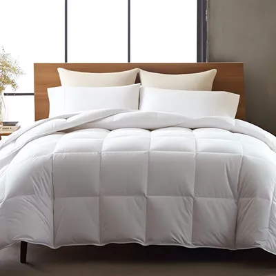 A white down comforter is neatly arranged on a bed with pillows and a wooden headboard.