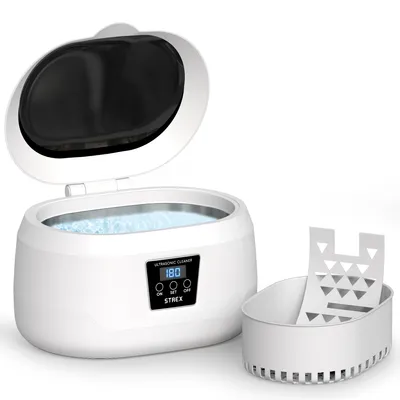 A white ultrasonic cleaner with its lid open, showing the cleaning basin filled with blue liquid. A white basket accessory is placed next to it. The product has a digital display and control buttons.