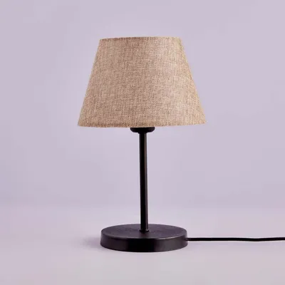 A table lamp with a beige fabric shade and a black metal base and stem, set against a light gray background.