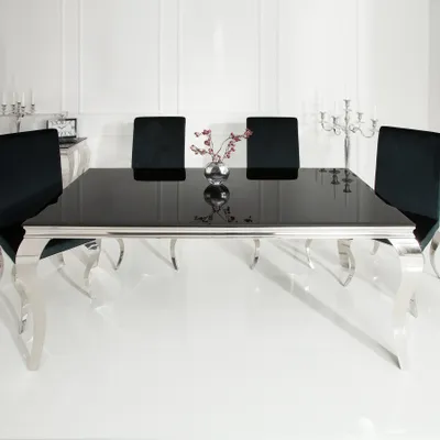 A modern dining table with black glass top and silver legs, set in a clean, white room with black chairs.