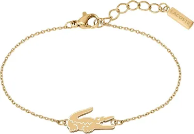 A gold-colored bracelet with a crocodile charm and a small rectangular tag with the Lacoste logo.