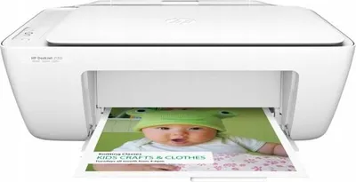 A white HP Deskjet 2130 printer is shown from the front, printing a picture of a baby.