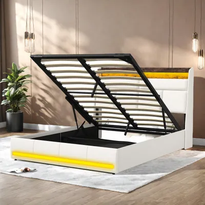 A white upholstered bed frame with the storage mechanism open, revealing the slatted base. Yellow LED lighting is visible along the bottom of the frame.