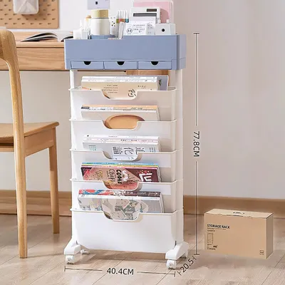A white and blue rolling storage cart filled with books and magazines, next to a wooden chair and desk. A cardboard box with 'STORAGE RACK' printed on it is visible in the lower right corner.