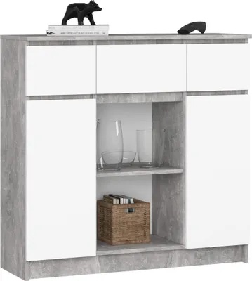 A modern kommode with white doors and a concrete-effect frame, displaying some glassware and a basket on shelves.
