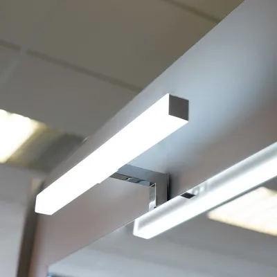 A close-up view of a modern LED light fixture mounted above a reflective surface, likely a mirror.