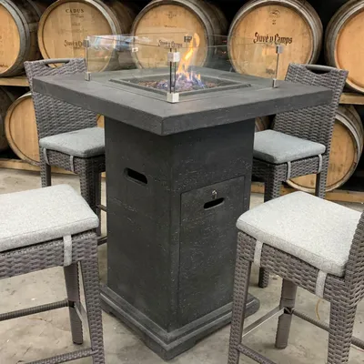 A gas fire pit table with chairs in a rustic setting with wine barrels in the background.
