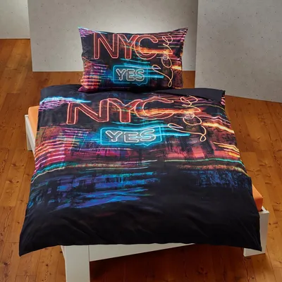 A duvet cover and pillowcase set with a neon NYC cityscape design is displayed on a bed.