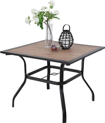 A square outdoor table with a wood-like top and black metal legs, decorated with a vase of white flowers and a black lantern.
