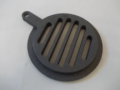 A dark gray cast iron grate with a handle and a circular base is placed on a light gray surface.