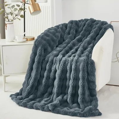 A dark gray plush blanket draped over a white chair next to a white cabinet with a lamp and a vase.