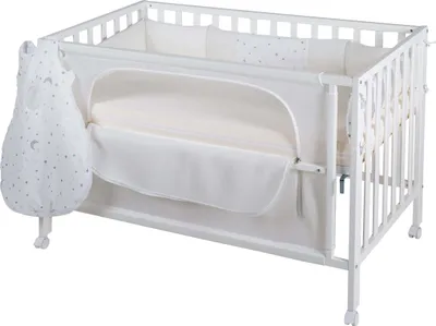 A white crib with bedding and a hanging sleeping bag.