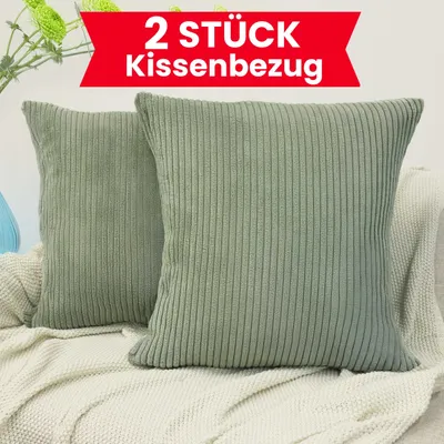 Two green corduroy pillow covers are displayed on a textured white blanket, with a hint of greenery and a blue vase in the background.