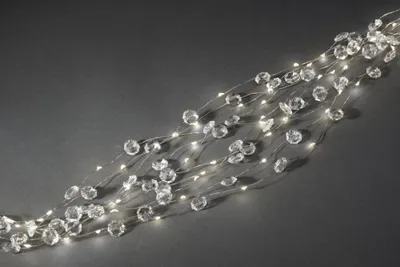 A string of clear, faceted beads and warm white LED lights on thin silver wires, laid out diagonally on a dark gray background.