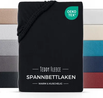 A black fitted sheet is shown with a stack of other colored fitted sheets in the background. There is text and a logo on the black sheet.