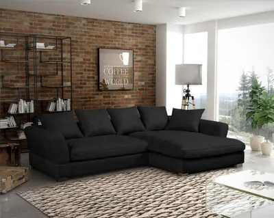 A modern living room with a black sectional sofa, brick wall, and large windows.