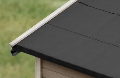 A close-up view of the corner of a shed roof, showing the black bitumen roofing material and a white trim.