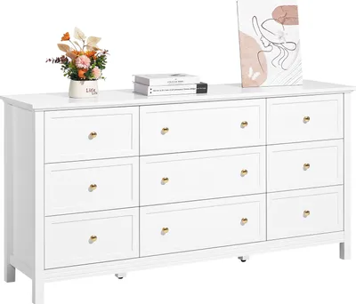 A white dresser with nine drawers, decorated with a vase of flowers and books on top.