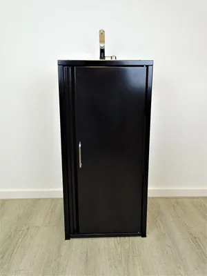 A black cabinet with a silver faucet on top, set against a white wall and a wooden floor.