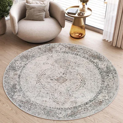 A round rug with a vintage design is placed on a wooden floor in a living room setting, next to a modern armchair and a side table.