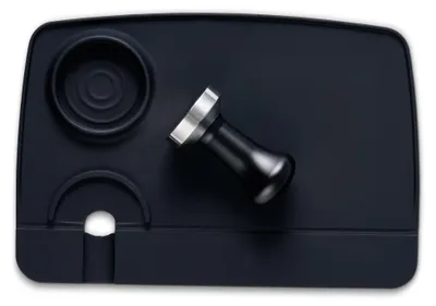 A black silicone tamper mat with a coffee tamper resting on it.