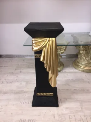 A decorative black pedestal with gold accents stands on a light-colored floor.