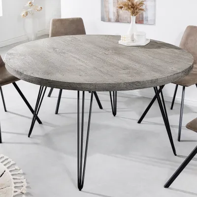 A round dining table with a gray wood-look top and black hairpin legs, shown in a dining room setting with chairs.