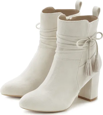 A pair of beige ankle boots with tassels and decorative lacing.